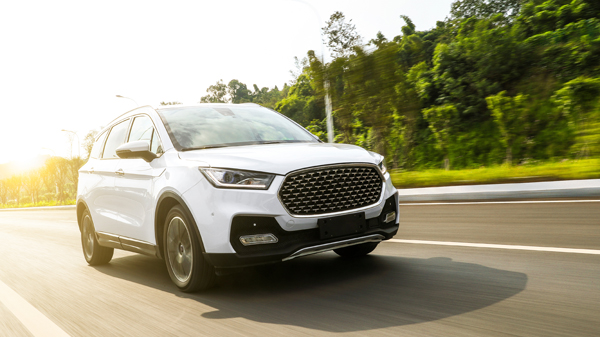 Late model white SUV driving down highway with trees in the background.