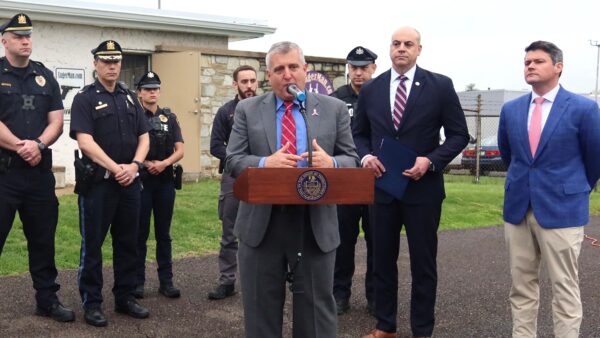 Farry speaking at podium alongside AG Sunday. Rep. Hogan and law enforcement officials.