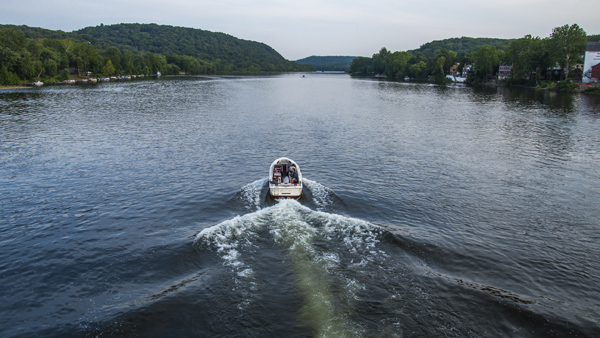 Midsized boat traveling through the middle of a lake with trees and mountains in the background.