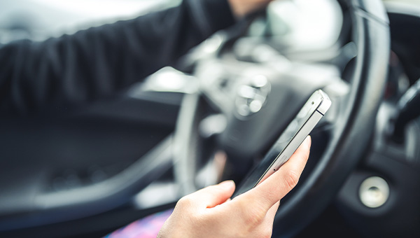 [Left hand on car steering wheel while driver holds cellphone in right hand.