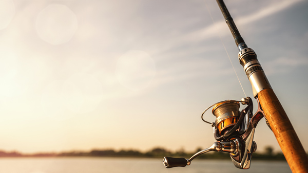 Fishing pole with reel in foreground and lake and sky in background.