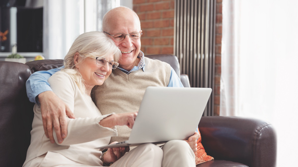 Man and woman sitting close on sofa while working on laptop.
