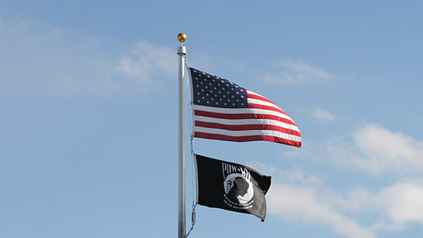 U.S. flag on flag pole with POW/MIA flag underneath set against blue sky