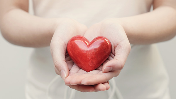 Female hands cupping a red, heart-shaped object.