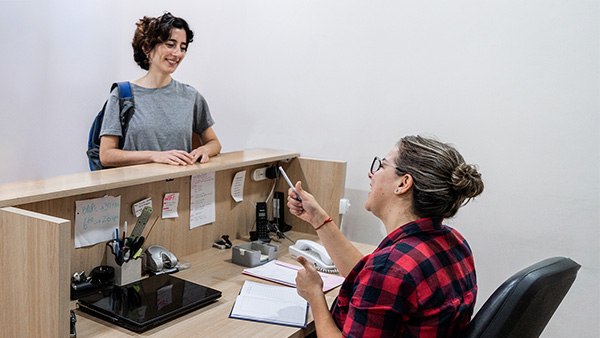 Student standing at office counter speaking to seated office worker.