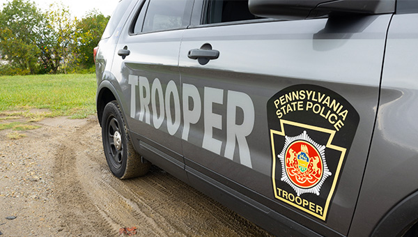 Vehicle parked on mud and grass with wording on door reading “Pennsylvania State Police Trooper.”