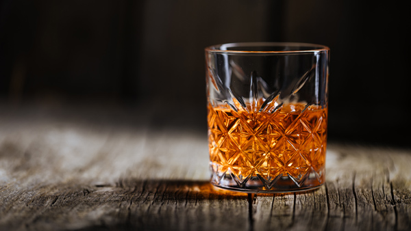 One glass of whiskey or brandy in a glass with dramatic light on an old wooden table.