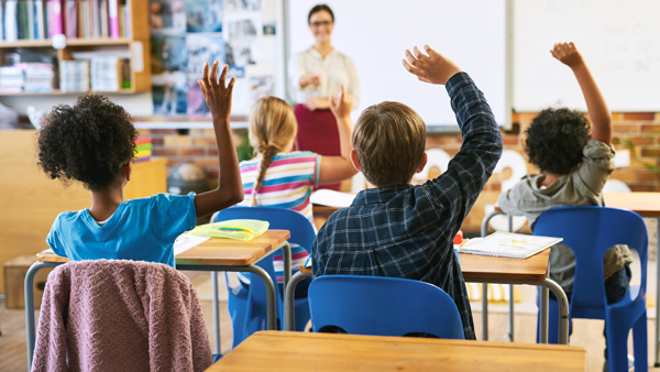 Education, question with group of children in classroom and raise their hands to answer. Learning or support, diversity and teacher teaching with young students in class of school building together.
