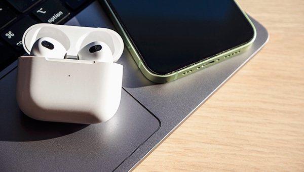 White wireless bluetooth headphones with green smartphone on laptop on wooden background.