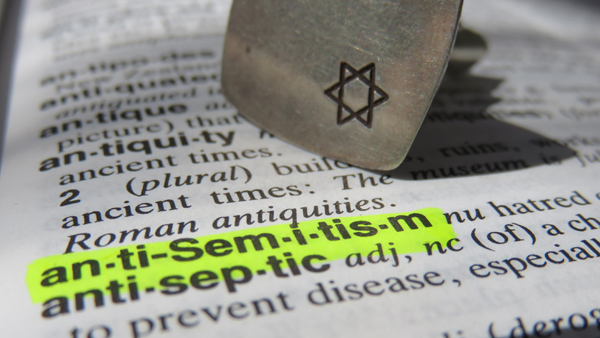 Open page of a dictionary turned to the word “anti-Semitism” with a Jewish star pin on the page