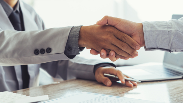 Closeup of two men in business attire shaking hands over a desk.