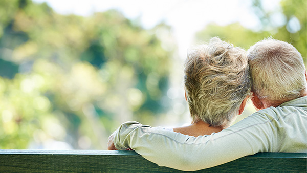 Man and woman with gray hair sitting close together on park bench.