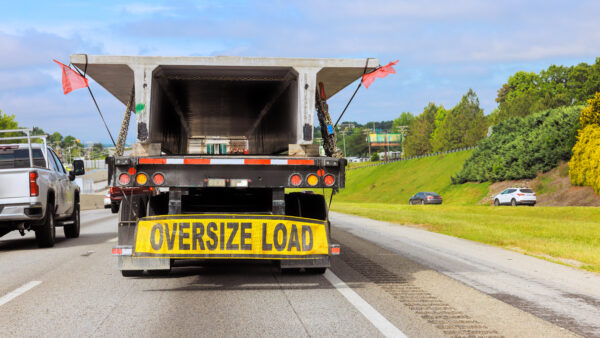Large truck equipped with an oversize load sign drives along busy highway under transportation in motion.