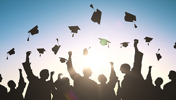 College graduates in gowns tossing graduation caps into the air, set against blue sky