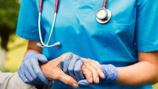 Nurse in blue scrubs holding the hands of her elderly patient.