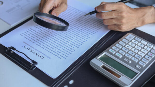 Business professional carefully reviewing a legal document and contract using a magnifying glass.