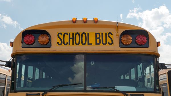 Front view of yellow school bus, featuring red and amber lights, windshield and the word “School Bus.”