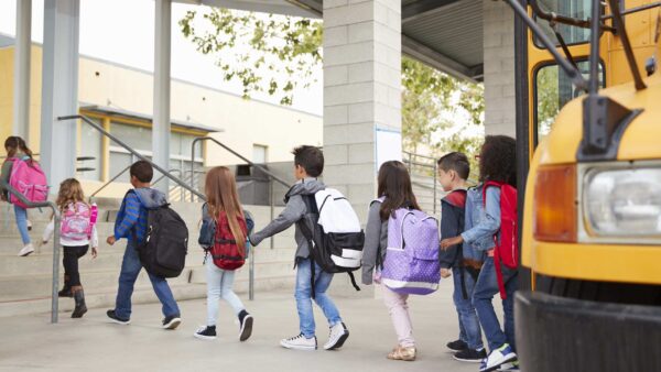 Children stepping off a school bus and walking into school.